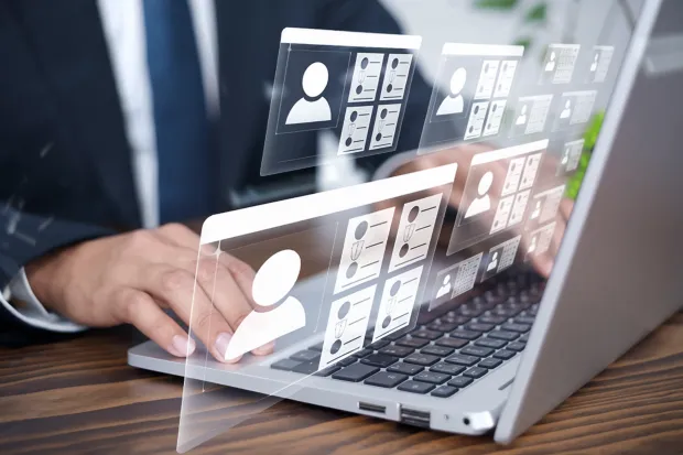 A person in a business suit typing on a laptop, with digital identity profile icons and user interface elements hovering above the keyboard, representing user management or identity access systems.