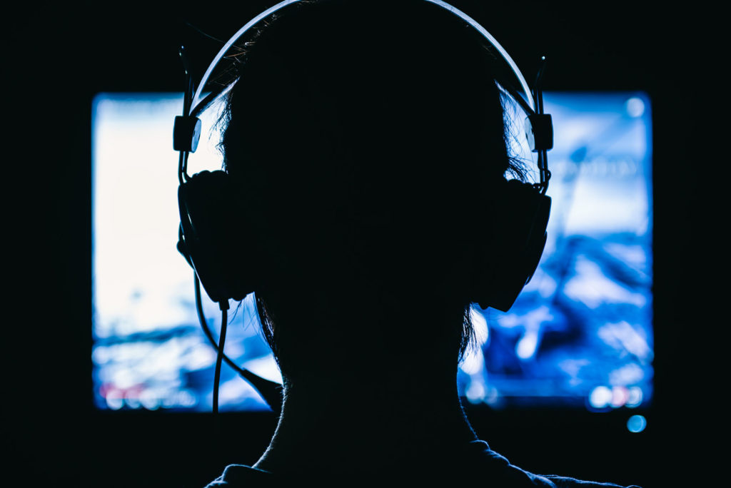 Woman gamer with headset facing a video game screen.